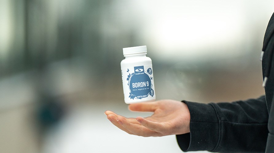 Billedet viser en h�nd, der kaster produktet Healthwell Boron 9 op i luften. Baggrunden er sl�ret.